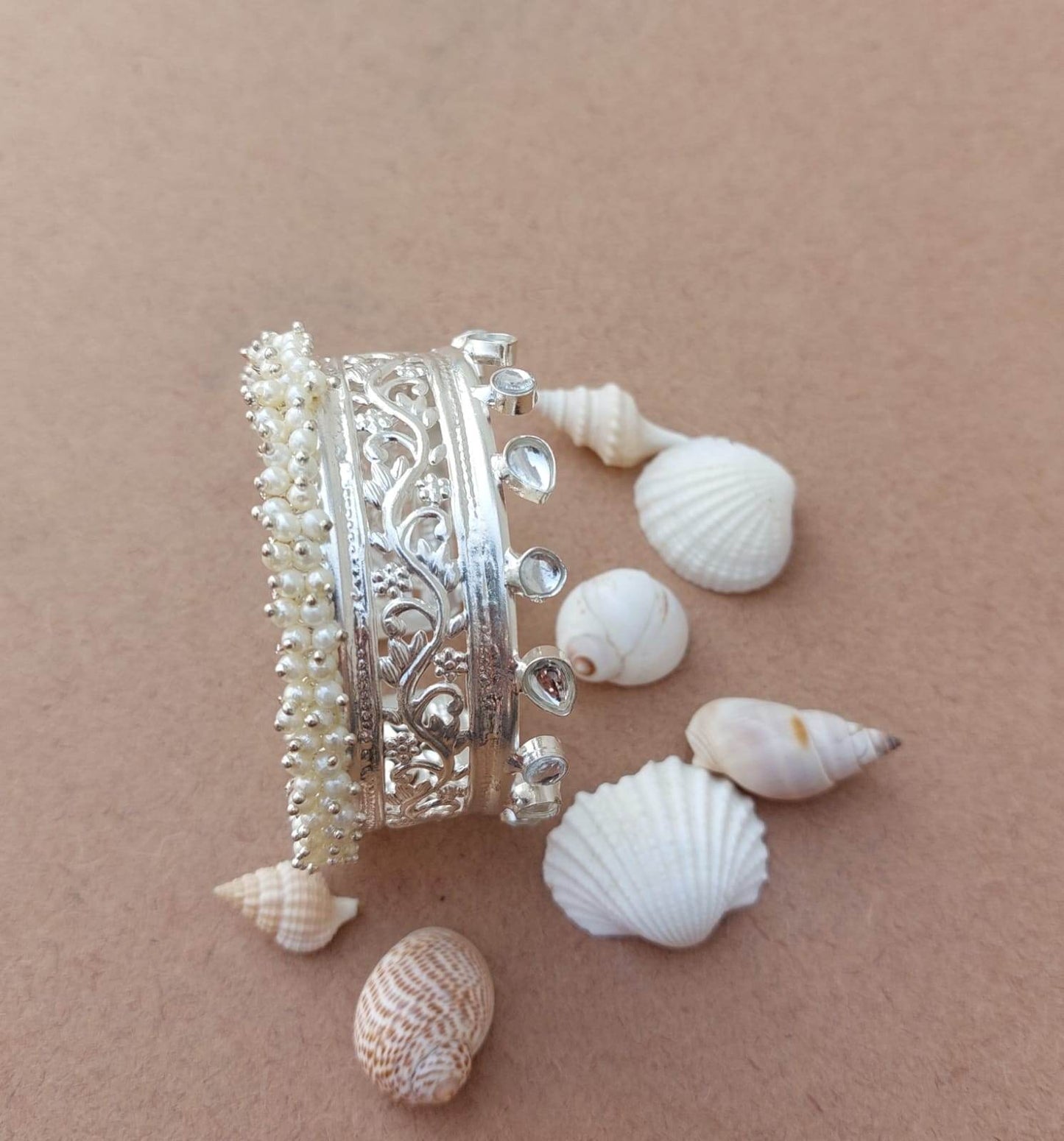 silver look alike handcuff bangles emblished with kundan & pearl, and also shows small conch in back ground.