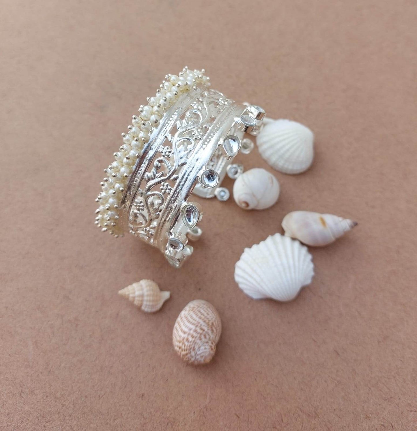silver look alike bangles emblished with kundan & pearl, and also shows small conch in back ground.