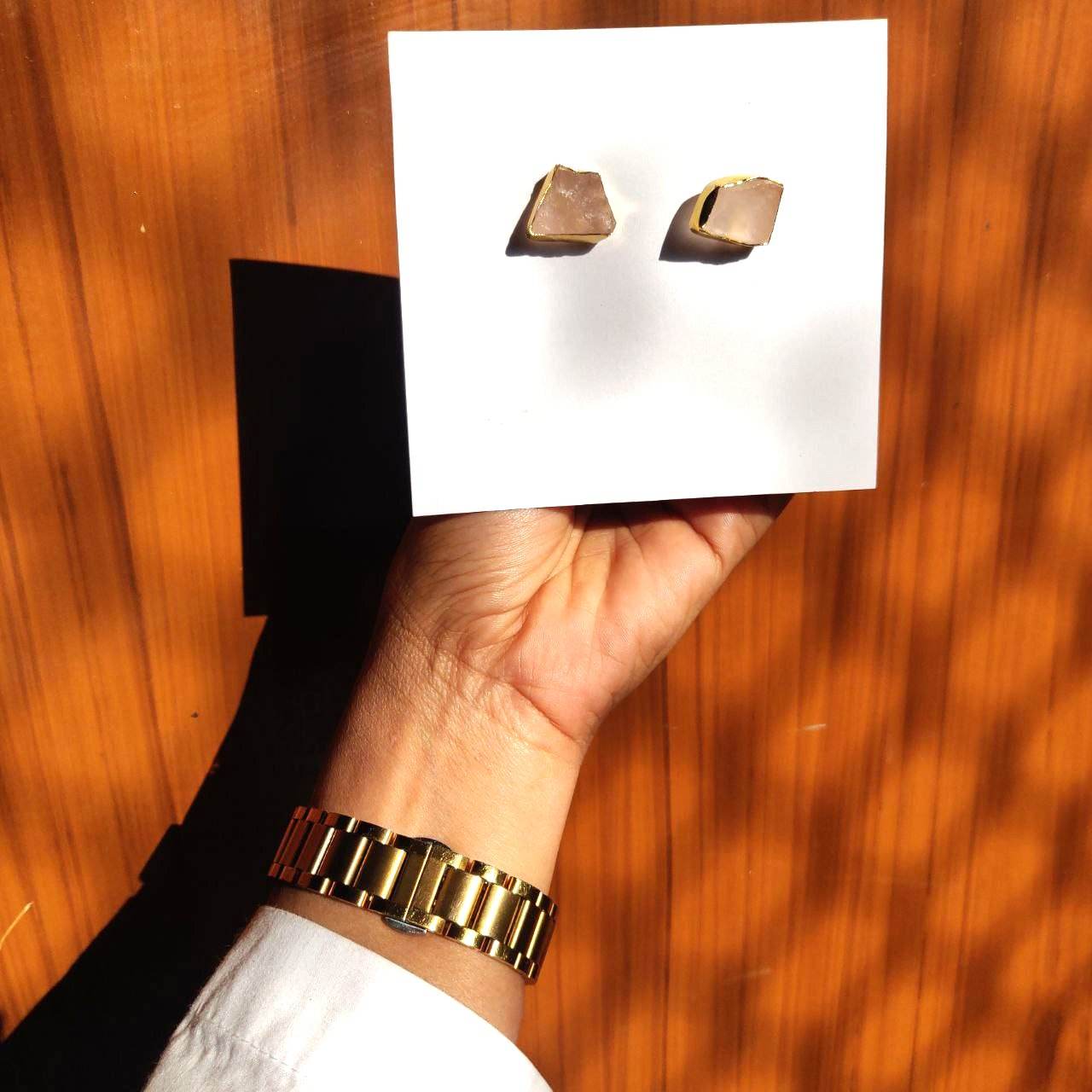 A lady shows gold-plated semi-precious gemstone earring studs on her hand in rose quartz color.