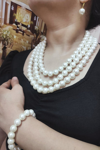 A lady is wearing a shell pearl necklace with matching earrings and bracelet