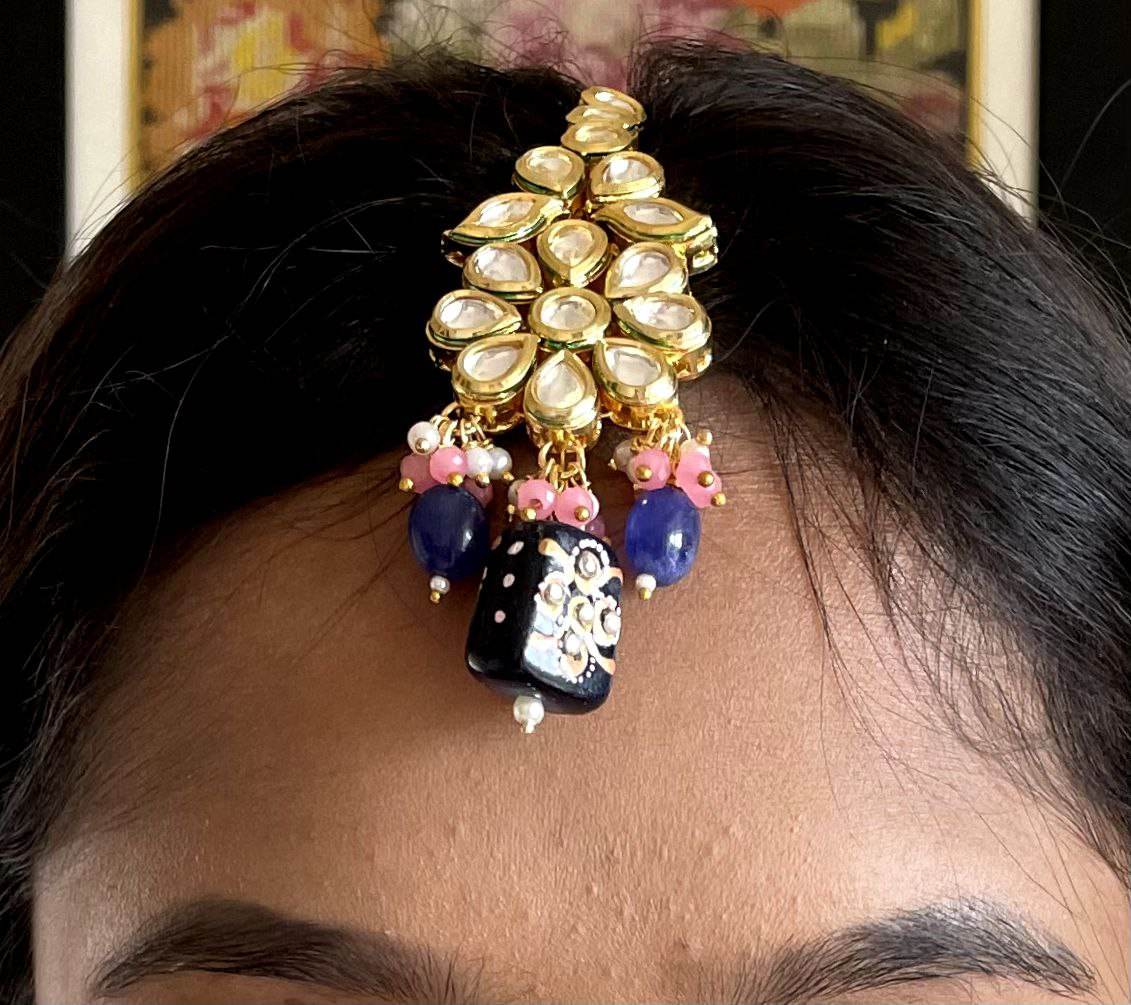 A lady is wearing blue maang tikka on the head